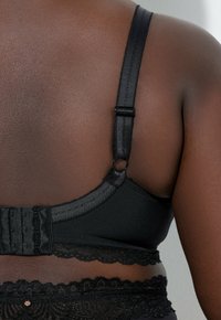 Svart bh med justerbara band, hysk- och hakspänne samt spetsdetaljer längs bandet. Tillverkad av mjukt, texturerat tyg.