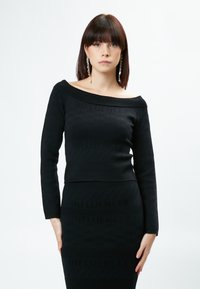 Schwarzes zweiteiliges Outfit bestehend aus einem taillierten, schulterfreien Langarmoberteil mit strukturierten Mustern und einem passenden Rock mit dem Textdetail "INFLUENCER".