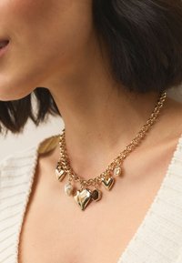 Gold chain necklace featuring multiple heart-shaped pendants and a single pearl accent. Textured links and a smooth finish on the charms.