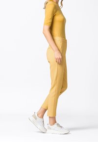 Žlutý top s krátkými rukávy a hladkou texturou, kombinovaný se vzorovanými žlutými kalhotami a bílými teniskami s textura designem.