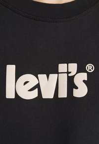 Gros plan sur un tissu noir avec un grand logo blanc de la marque Levi's imprimé au centre de la poitrine d'un vêtement.