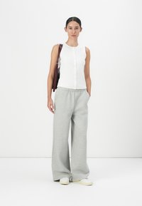 White sleeveless top with button details, gray wide-leg pants, and white sneakers. A dark bag is slung over one shoulder.