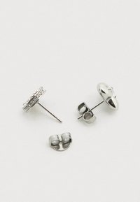 Boucles d'oreilles clous en argent avec un design circulaire, ornées de petites pierres claires, et une tige avec fermoir papillon.