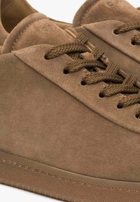 Brązowe zamszowe sneakersy z okrągłymi sznurowadłami, gładką teksturą i gumową podeszwą z lekkim odcieniem kontrastującym wzdłuż krawędzi.