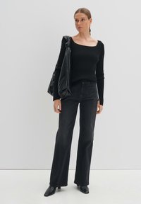 Schwarzer, gerippter Strickpullover mit quadratischem Ausschnitt, kombiniert mit hoch taillierten, schwarzen, ausgestellten Jeans. Abgerundet wird der Look durch schwarze, hochhackige Stiefeletten.