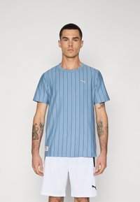 Lichtblauwe korte mouwen t-shirt met verticale strepen, ronde hals en een klein gouden Puma-logo op de borst. Gekenmerkt met witte shorts.