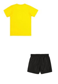 Camiseta de algodón amarilla de manga corta, con un cuello en barco. Combinada con pantalones cortos negros de tela suave con una cinturilla elástica.