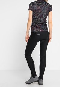 Kortärmad, åtsittande topp med ett flerfärgat geometriskt mönster, kombinerad med tajta svarta leggings med GORE-logotyp. Svarta träningsskor.