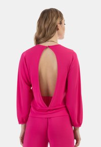 Top rosa aderente con maniche lunghe e un profondo taglio sulla schiena. Il tessuto è morbido e un bottone decorativo caratterizza il collo.