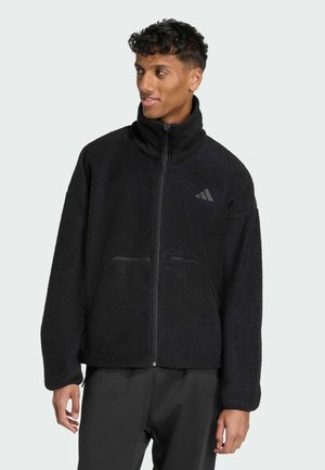 Black fleece jacket with high collar, zip closure, and front pockets. Features a subtle dark logo on the chest and a textured surface.