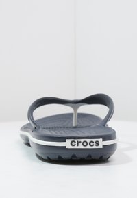 Tume sinine sussikes, millel on tekstureeritud tallad, paindlikud rihmad ja valge aksentjoon. Jalal on "crocs" logo.