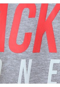 Tessuto grigio con grandi testi rossi e bianchi e una superficie leggermente texture. Le lettere sono in grassetto e prominenti, enfatizzando il design.