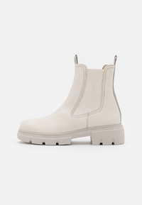 Krémová kožená Chelsea bota s masivní podrážkou, elastickými bočními panely a poutky na bílém pozadí, boční pohled.