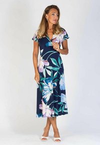 Navy sininen kukkamekko midi-pituudella, jossa on lyhyet röyhelösoftaat. Mekossa on suuria vaaleita kukkia, V-mallinen kaula-aukko ja ilmava hame. Yhdistetty valkoisten sandaalien kanssa.