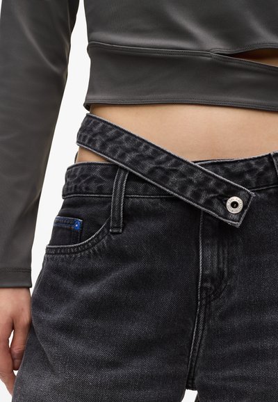 Jean en denim foncé avec une ceinture large et texturée. Comprend un bouton en argent et un accent bleu sur la poche. Le matériau semble durable et légèrement usé.
