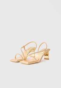Gold slingback heels with a square toe, featuring a metallic finish and thin straps adorned with rhinestones. Square, block heel design.