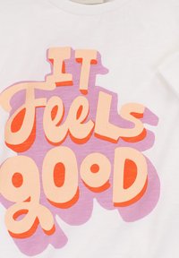 Wit katoenen T-shirt met kleurrijke tekst: "IT FEELS GOOD" in oranje en roze, met een gestructureerd, gelaagd effect.