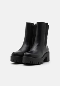 Botas de tobillo de cuero negro con plataforma gruesa y suela con tacos. Presentan paneles laterales elásticos para un fácil uso y un acabado suave.