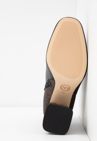Semelle d'une botte cheville marron avec une semelle extérieure beige texturée, talon noir, fermeture éclair sur le côté, et taille 6M indiquée près du logo de la marque.