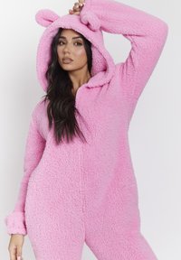 Body in pile rosa con cappuccio, caratterizzato da orecchie d'orso e una zip frontale. Materiale morbido e strutturato con maniche e gambe a costine.