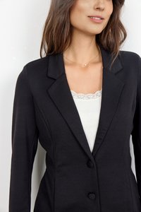 Schwarzer taillierter Blazer mit Reversschlägen, zwei Knöpfen und glatter Textur. Über einem weißen gerippten Camisole mit Spitze getragen.