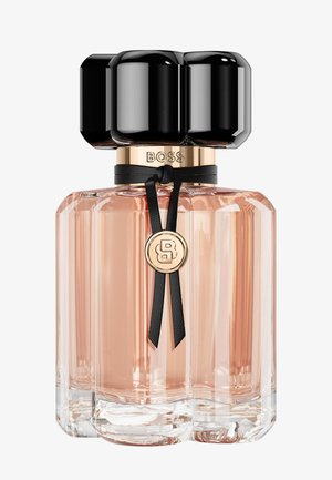 Glas parfume flaske med lyserød væske, sort rundet låg, guld krave indgraveret med "BOSS," og sort bånd med guldemblem.