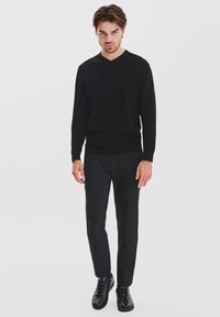 Czarny dzianinowy sweter z dekoltem w serek, zestawiony z dopasowanymi czarnymi spodniami i czarnymi trampkami, wszystko w minimalistycznym stylu na neutralnym tle.