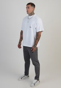 Camiseta blanca de manga corta con un pequeño logo, combinada con pantalones gris ajustados con bolsillos y zapatillas blancas con detalles grises.