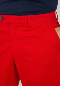 Rode shorts van lichte stof met een vlakke voorkant, knoopsluiting en zijzakken. Soepele textuur met minimale details.