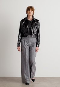 Fekete, fényes, rövidített dzseki két elülső zsebbels, magas derekú, bőszárú szürke nadrággal és hegyes orrú fekete cipőkkel párosítva.