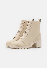 Stivali ankle in pelle beige con tacco a blocco, punta rotonda, chiusura con lacci e un accento grigio a contrasto sul tacco. Superficie testurizzata con dettagli di cucitura.