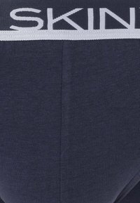 Slip di cotone blu navy con un elastico bianco in vita che riporta la scritta "SKIN." Il tessuto ha una texture liscia e una vestibilità aderente.