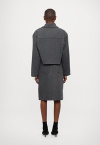 Giacca in denim grigia con design corto, maniche oversize e gonna a tubino abbinata. Presenta due tasche posteriori e un colletto strutturato.