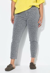 Jeans de estampado de leopardo gris con corte entallado y longitud hasta el tobillo, hechos de mezclilla. Combinados con zapatos marrones tipo slip-on y un suéter de punto amarillo.