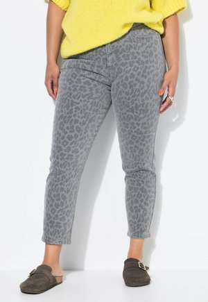 Jeans in stampa leopardata grigia con taglio taper e lunghezza alla caviglia, realizzati in denim. Abbinati a scarpe slip-on marroni e a un maglione giallo in maglia.