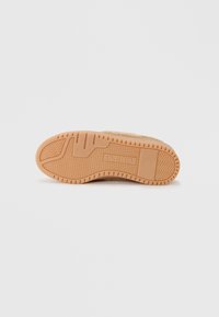 Semelle de sneaker en caoutchouc léger marron texturé, avec des motifs de semelle prononcés, un détail de logo et une forme lisse et contourée.