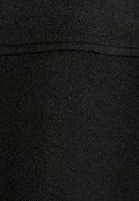 Černá texturovaná tkanina s měkkým, chlupatým vzhledem, s hladkým švem probíhajícím horizontálně přes povrch.