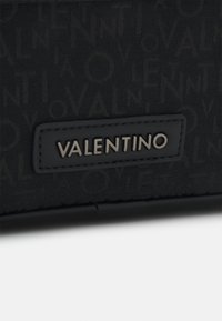 Black fabric wallet featuring an embossed logo pattern, a smooth leather accent with the text "VALENTINO" in metallic lettering.