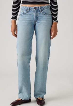Personne portant un jean bleu clair droit, un crop top rayé noir et blanc à manches longues, et des chaussures marron foncé.