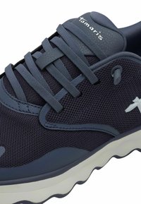 Marinefarbene Mesh-Sportschuh mit strukturierten Einsätzen, flachen Schnürsenkeln und einer weißen Gummisohle mit wellenförmigen Mustern. Markenlogo an der Seite.
