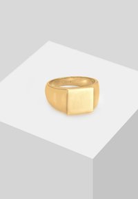 Guldtonet ring med en glat, rundet bånd og en fremtrædende firkantet front med en poleret overflade, monteret på en lysegrå platform.