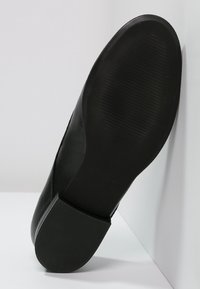 Czarny skórzany but z lekko zaokrąglonym czubkiem i teksturowaną gumową podeszwą. Podeszwa ma poziomy wzór żłobień dla lepszej przyczepności.