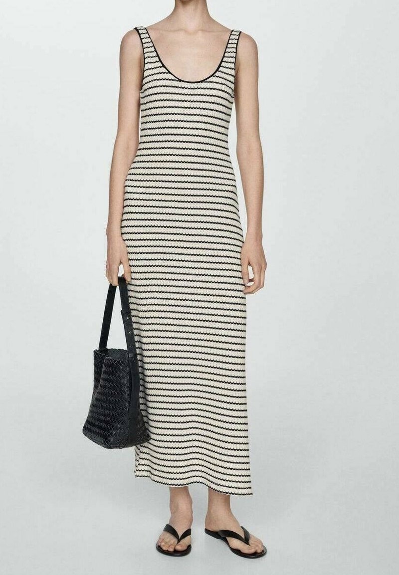 Femme portant une robe maxi sans manches rayée noir et blanc, tenant un sac à main noir tressé et portant des sandales plates noires.