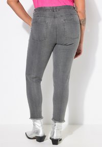 Jeans skinny de denim gris con una cintura alta, que cuentan con dos bolsillos traseros y un dobladillo deshilachado. Combinados con botas de tobillo plateadas y brillantes.