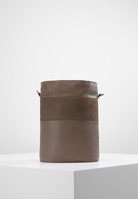 Borsa a secchiello rotonda realizzata in pelle marrone, con una texture liscia, una fascia orizzontale ampia e un design pulito e minimalista.