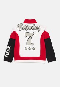 Rød og hvit jakke med høy krage, svarte ermer og et stort "Replay 7"-grafikk med stjerner på baksiden. Mykt stoff, sporty design.