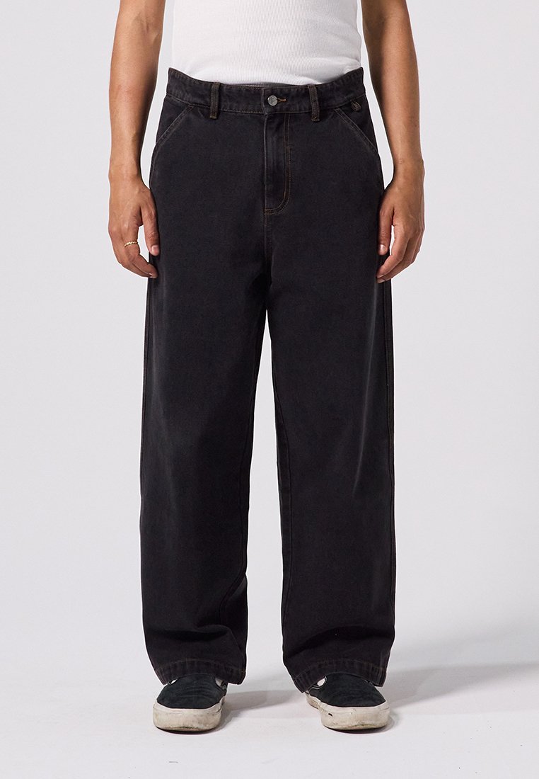 Pantalon en denim noir à coupe ample, doté d'une fermeture à boutons, de cinq poches et de coutures contrastées. Le tissu est robuste avec une texture lisse.