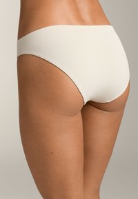 Belični bikini z gladko teksturo in širokim pasom, ki prikazuje nizko postavitev in minimalno pokritost.