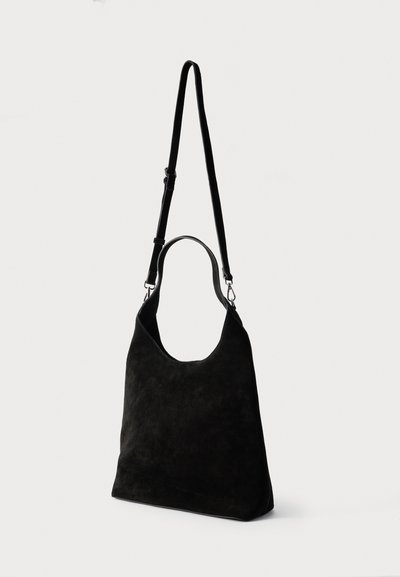 Μαύρη σουέντ τσάντα ώμου με κοντή λαβή και ρυθμιζόμενο μακρύ λουρί σε απλό λευκό φόντο.