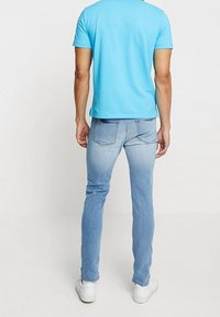 Maglietta azzurro chiaro con scollo rotondo, abbinata a jeans a lavaggio chiaro. I jeans presentano un effetto usurato e tasche posteriori. Sneakers bianche.